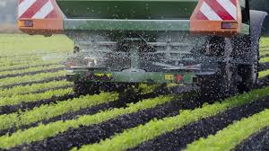 Tractor spreading fertiliser across a crop field